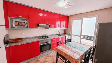 Una cocina con armarios rojos, estufa a gas, pileta y una mesa de comedor con sillas.