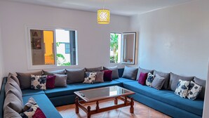 Una sala de estar con un sofá seccional azul, una mesa de centro de madera y un ventanal con contraventanas.