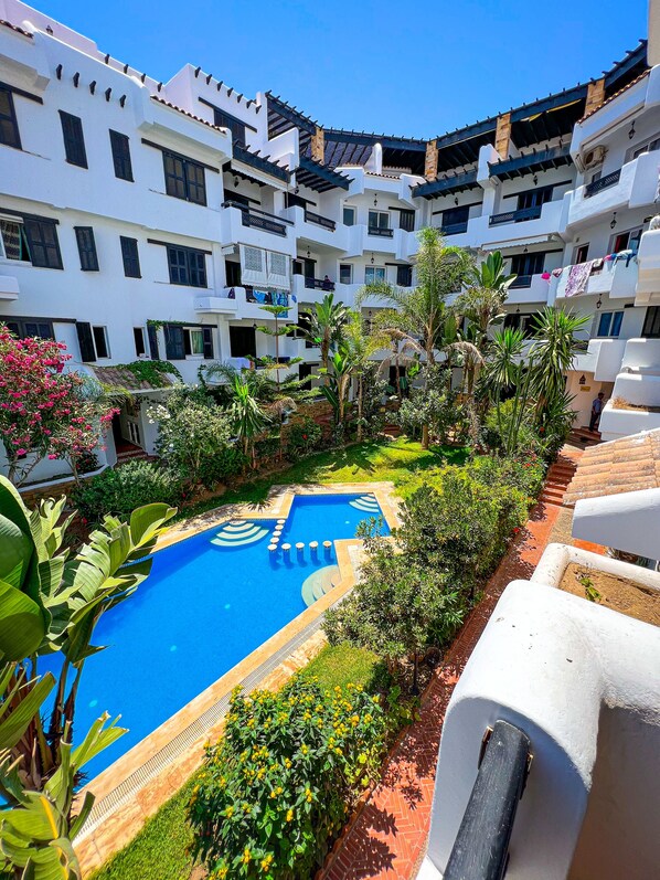 A courtyard with a swimming pool surrounded by lush greenery and white buildings with balconies. - Visit Oued Laou: Jawhara (Oued Laou)