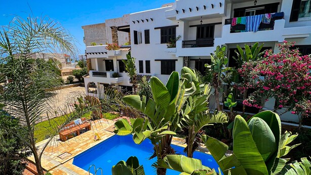 Un edificio moderno con balcones, piscina y abundante vegetación.