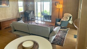 A cozy living room with a sofa, a coffee table, and a chair. There is a lamp and a window with a view of the outdoors.