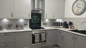 A modern kitchen with grey cabinets, a stainless steel range hood, a microwave, and a clock on the wall. - Harbourside, Luxury Two Bedroom Townhouse with Bike store – Sleeps 6 (Wick)