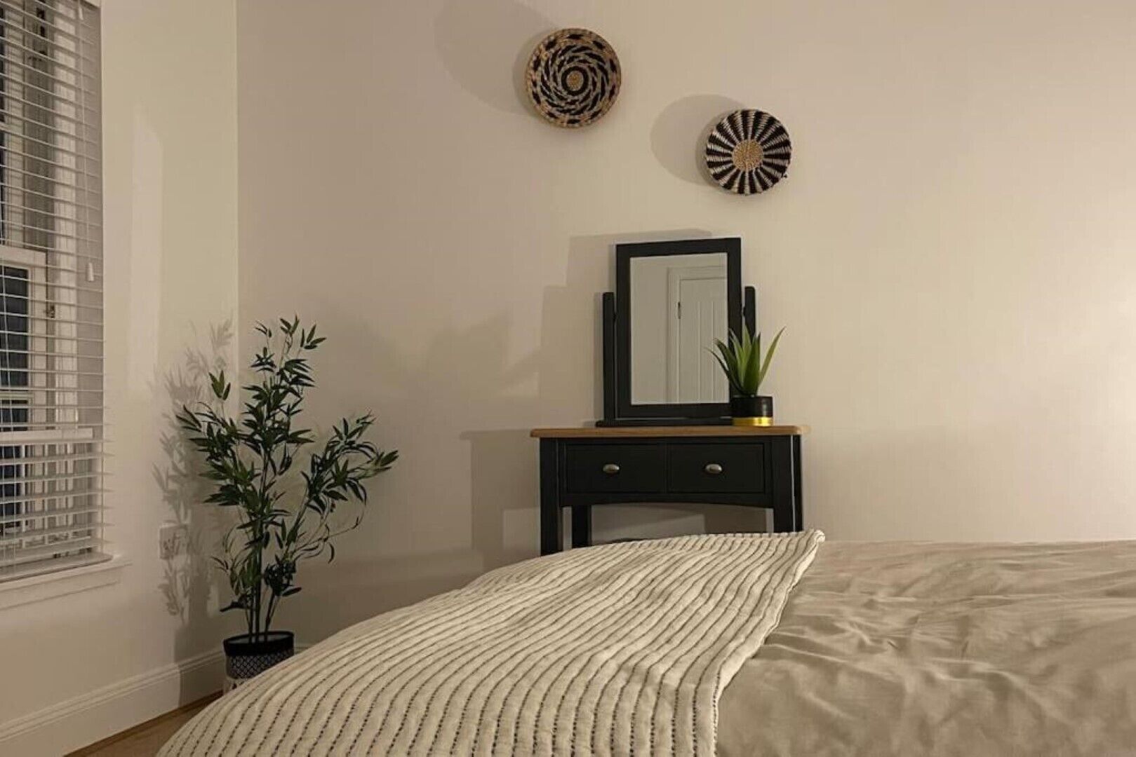 Een slaapkamer met een bed, een nachtkastje met spiegel, een potplant en wanddecoratie.