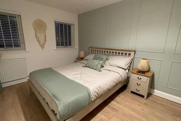 Un dormitorio con cama, mesitas de noche, un radiador y una ventana con persianas.