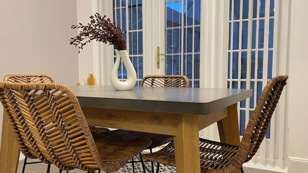 A dining table with four wicker chairs, a vase with dried flowers, and a window with white shutters in the background. - Harbourside, Luxury Two Bedroom Townhouse with Bike store – Sleeps 6 (Wick)