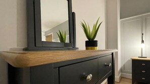 A dark wooden dresser with a mirror, a potted plant, and a lamp on a bedside table. - Harbourside, Luxury Two Bedroom Townhouse with Bike store – Sleeps 6 (Wick)