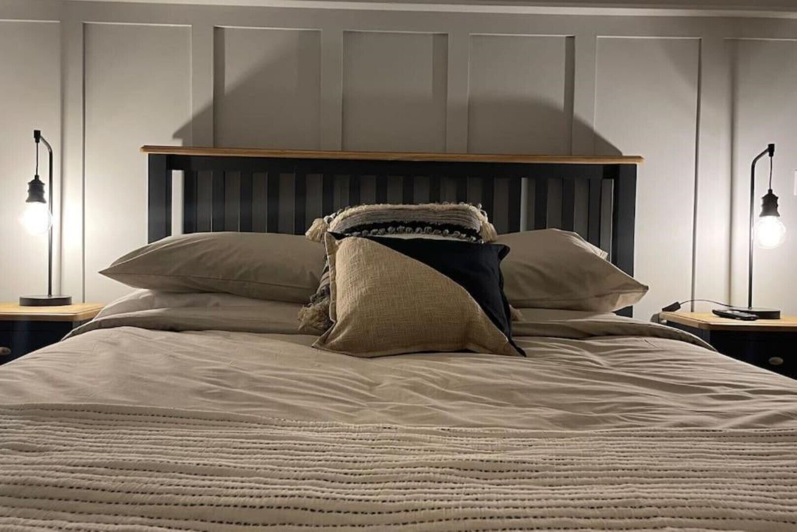 Ein Bett mit Holz-Kopfteil, zwei Nachttischlampen und einer Decke.