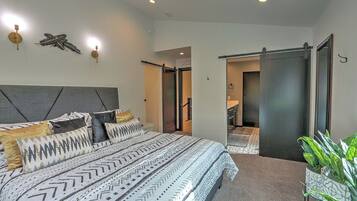 A modern bedroom with a large bed, a headboard, and a sliding door leading to a bathroom.