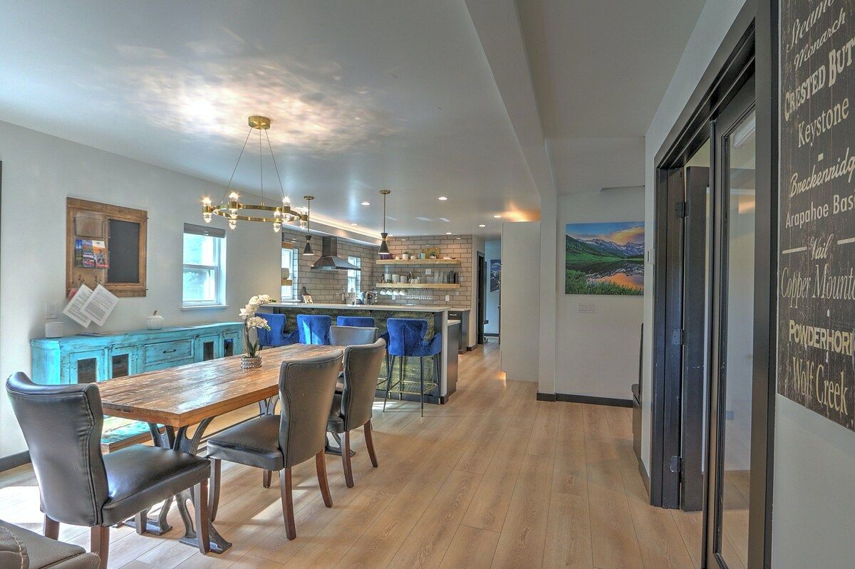 A modern kitchen with a central island, pendant lighting, and a dining area with a wooden table and chairs.