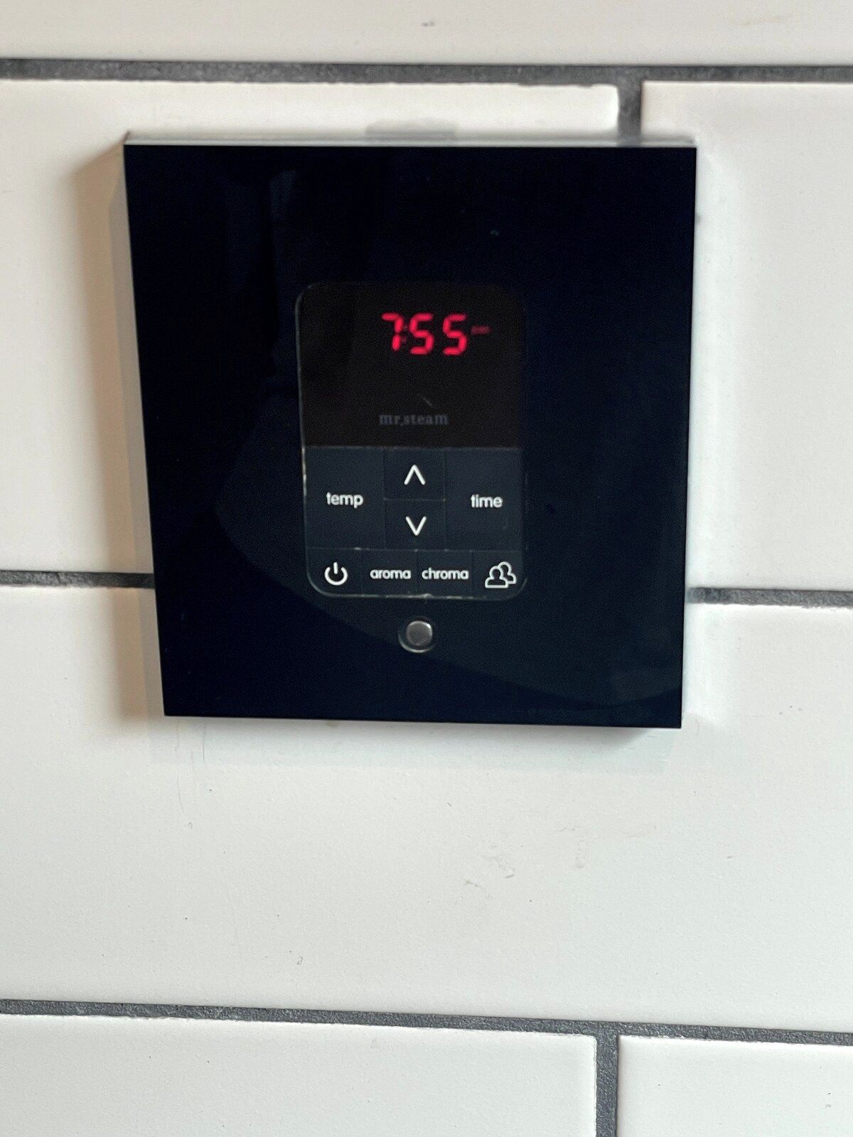 A digital thermostat mounted on a tiled wall.