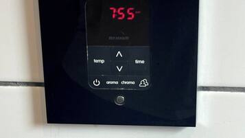 A digital thermostat mounted on a tiled wall.