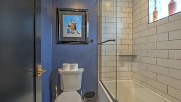 A bathroom with a toilet, a framed picture above it, and a shower area with white tiles.