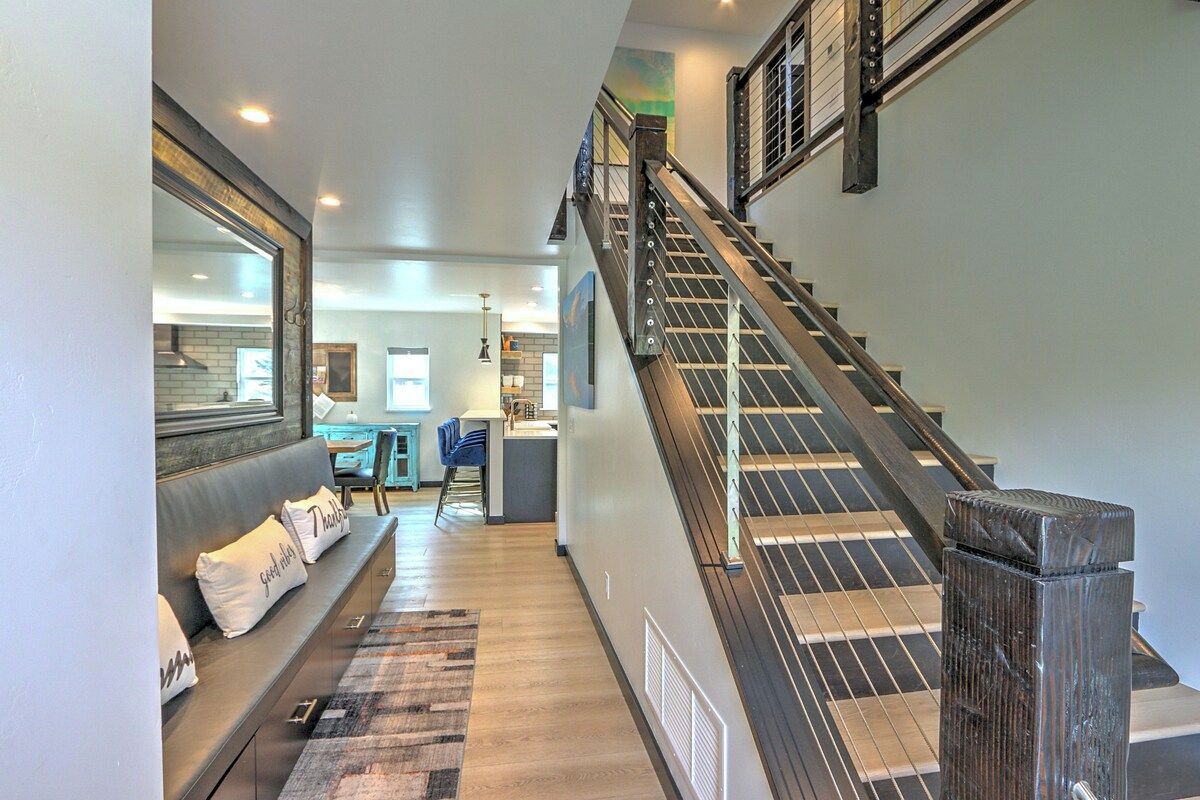 A staircase leading to an upper floor with a modern design, a seating area with a sofa and cushions, and a kitchen area in the background.