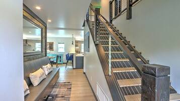 A staircase leading to an upper floor with a modern design, a seating area with a sofa and cushions, and a kitchen area in the background.