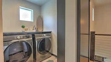 A laundry room with two front-loading washers and dryers, a small window, and a mirror on the wall.
