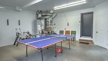 A ping pong table in a room with a door, a bicycle, and a wall-mounted air conditioning unit.