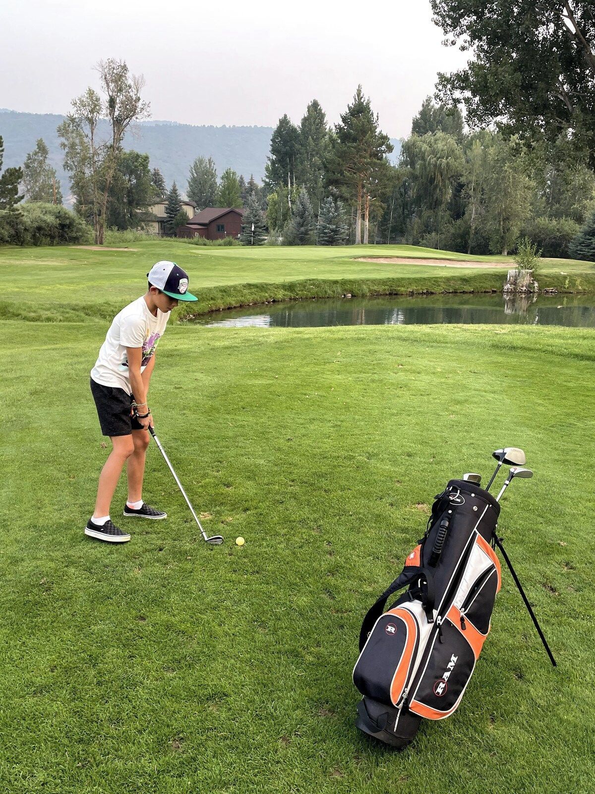 Ein Golfplatz mit einem Spieler, der sich zum Putt vorbereitet, einer Golfausrüstung und einem Teich im Hintergrund.