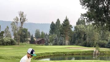 Ein Golfplatz mit einem Spieler, der sich zum Putt vorbereitet, einer Golfausrüstung und einem Teich im Hintergrund.