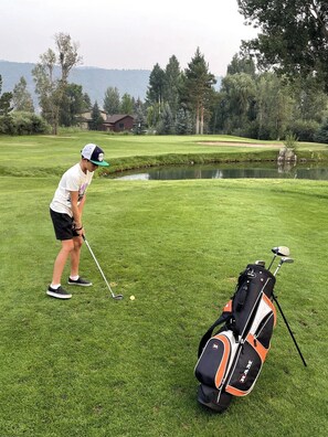 A golf course with a player preparing to putt, a golf bag, and a pond in the background.