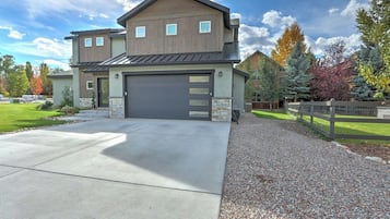 A two-story house with a garage, a driveway, and a gravel path leading to a wooden fence.