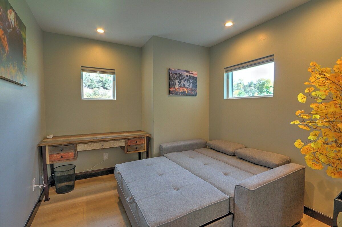A bedroom with a bed, a desk, two windows, and a wall-mounted artwork.