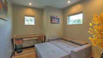 A bedroom with a bed, a desk, two windows, and a wall-mounted artwork.