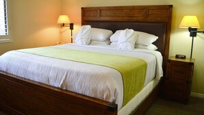 Ein ordentlich bezogenes Bett mit weißen Leinen und einer grünen Tagesdecke, daneben zwei Nachttischlampen und ein Nachttisch mit einer Schublade.