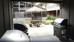 Eine Terrasse mit Grill, Tisch mit Sonnenschirm und einem Steinpflanzgefäß.