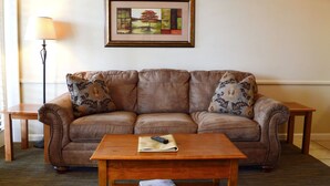 Ein braunes Ledersofa mit floralen Kissen, ein Couchtisch aus Holz mit Fernbedienung und Zeitschrift sowie ein gerahmtes Bild an der Wand.