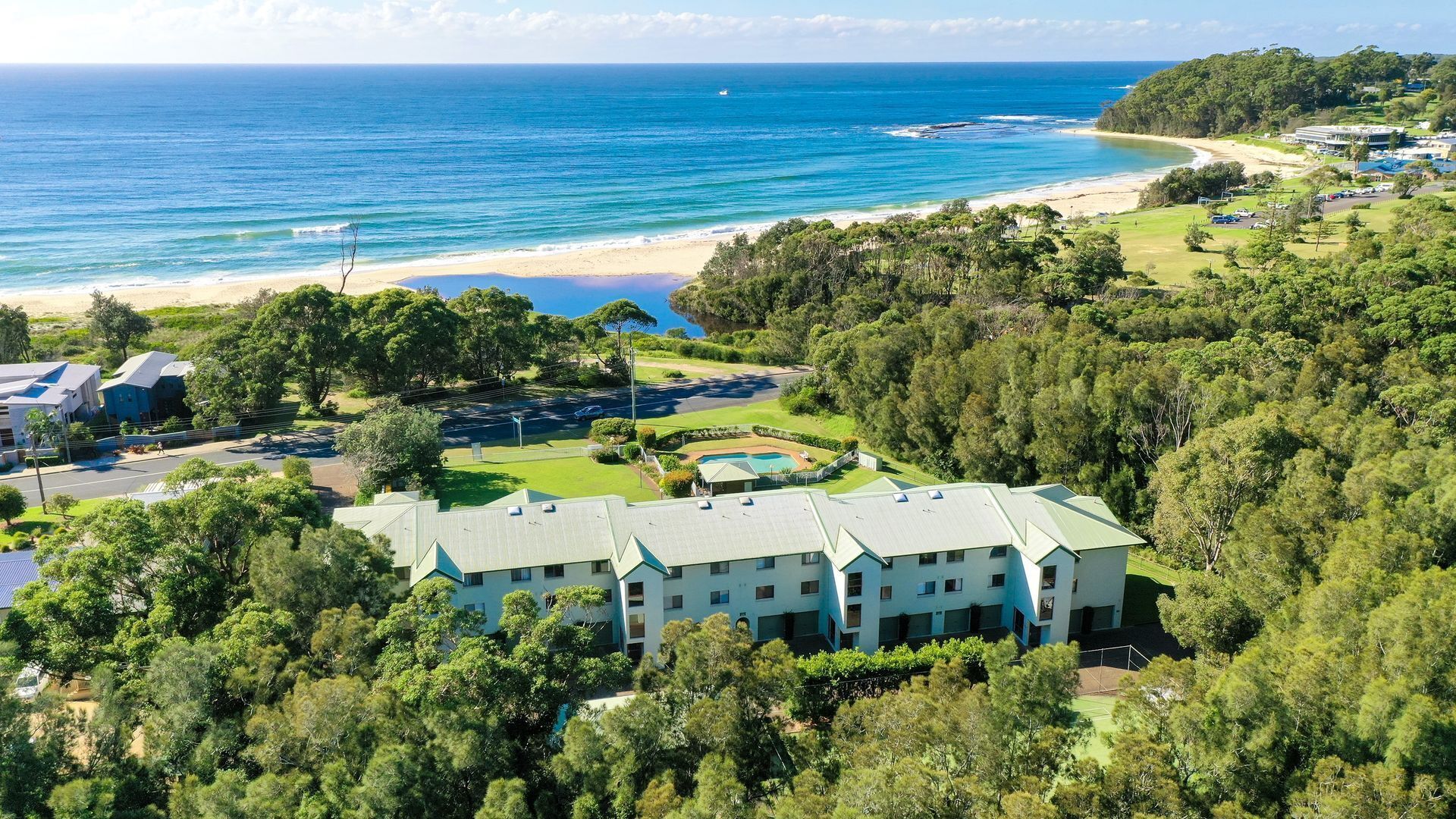 Een resort met zwembad, tennisbaan en uitzicht op het strand.