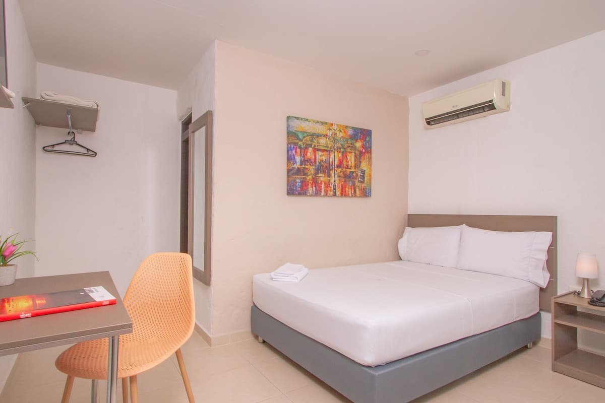 Une chambre d’hôtel avec un lit, un bureau et une chaise, un tableau au mur et un appareil de climatisation.