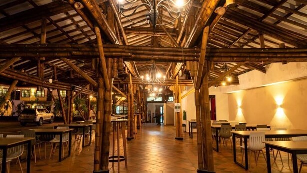 Un espacio interior con estructuras de bambú, mesas y sillas dispuestas para comer o socializar.