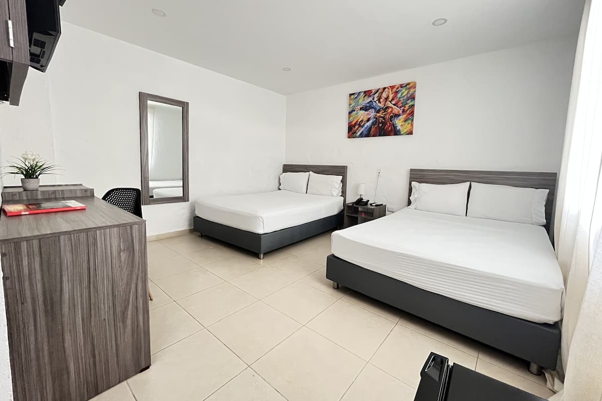 Une chambre d’hôtel avec deux lits, un bureau, un miroir, une plante en pot et un tableau coloré accroché au mur.