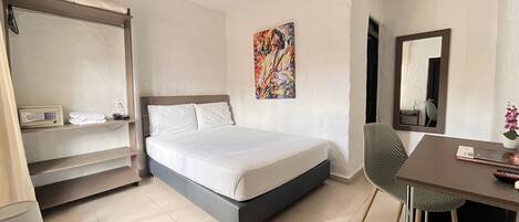 Een hotelkamer met een bed, een bureau, een stoel, een plank met een telefoon en een radio, een schilderij aan de muur en een spiegel.