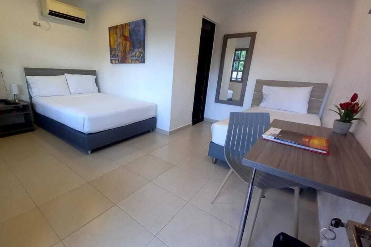 Une chambre d’hôtel avec deux lits, un bureau, une chaise, une petite table et une plante en pot.