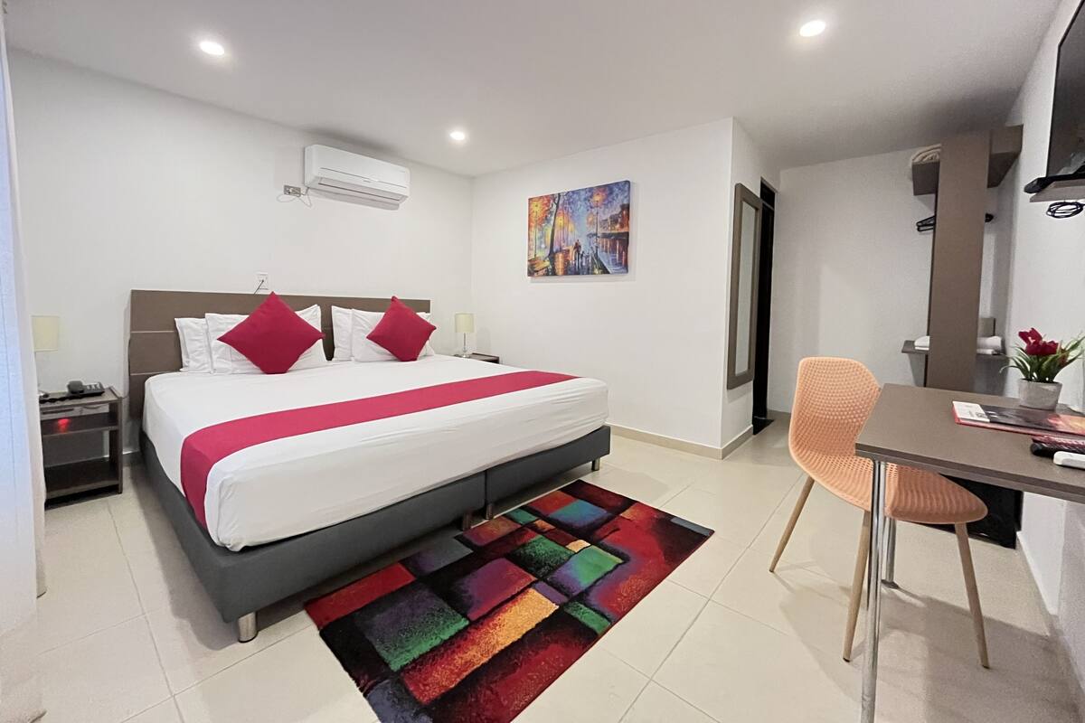 Une chambre d’hôtel moderne avec un grand lit, un bureau et un tapis aux couleurs vives.
