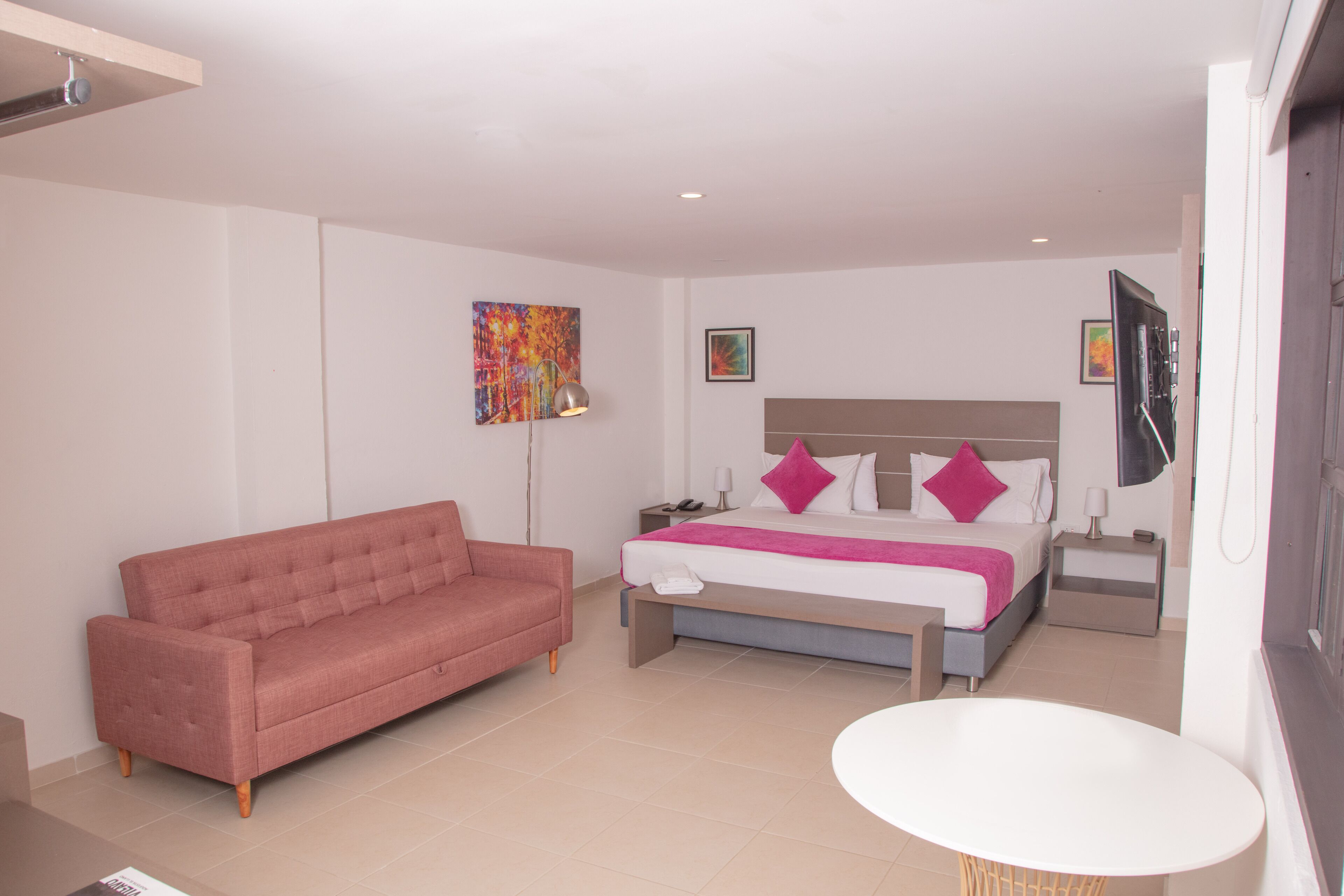 A modern hotel room with a bed, a sofa, a bedside table, and a small round table.