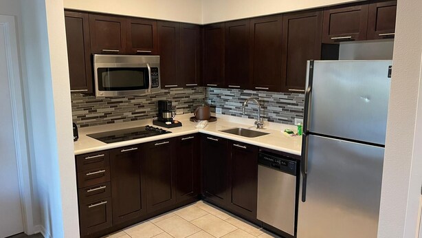 A compact kitchen with dark wooden cabinets, a stainless steel refrigerator, a microwave, and a coffee maker. - Pet friendly hotel aprt on Celebration Pl. 2bdr (Celebration)
