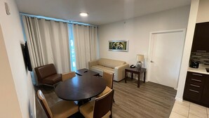 A modern living room with a round dining table, two sofas, a TV mounted on the wall, and a kitchen area with dark cabinets. - Pet friendly hotel aprt on Celebration Pl. 2bdr (Celebration)