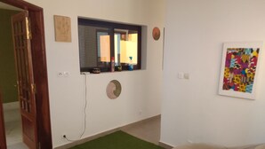 Una habitación con alfombra verde, un adorno circular en la pared, una ventana con espejo y una obra de arte colorida.