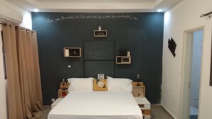 Un dormitorio con una cama sobre palets de madera, una pared oscura con una cita motivacional, mesitas de noche con lámparas y una ventana con cortinas.