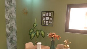Un comedor con una mesa de madera, sillas color beige, un jarrón verde con flores y un cuadro en la pared.