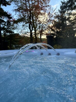 A hot tub with clear water flowing over its edge, surrounded by trees and a clear sky. -  Spectacular Lakefront Home- sleeps 20 ~ Hot Tub - Walk To Restaurants! (Lake Harmony)