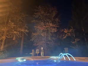 Un jacuzzi con una copa y una botella, rodeado de árboles por la noche.
