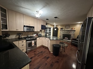 Una cocina moderna con armarios de madera, una isla central, estufa, microondas, refrigerador y chimenea de piedra.