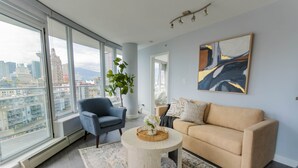 Una sala de estar moderna con un ventanal grande, un sillón azul, un sofá beige y una mesa de centro redonda con un florero.