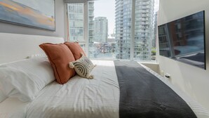 Una habitación de hotel moderna con una cama grande, televisión y vistas a edificios altos.