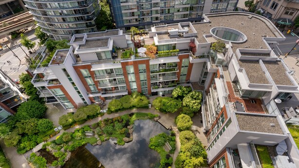 Un edificio moderno de varios pisos, con amplios ventanales y un patio central con un estanque y follaje.