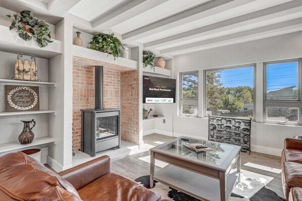 A modern living room with a fireplace, leather sofas, a glass coffee table, and a TV mounted on the wall. - Red Rock Farmhouse! Hot Tub, Fire Pit & Trails (Colorado Springs)