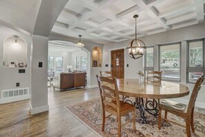 A spacious dining area with a round wooden table and chairs, a patterned rug, and a ceiling with exposed beams. - Red Rock Farmhouse! Hot Tub, Fire Pit & Trails (Colorado Springs)